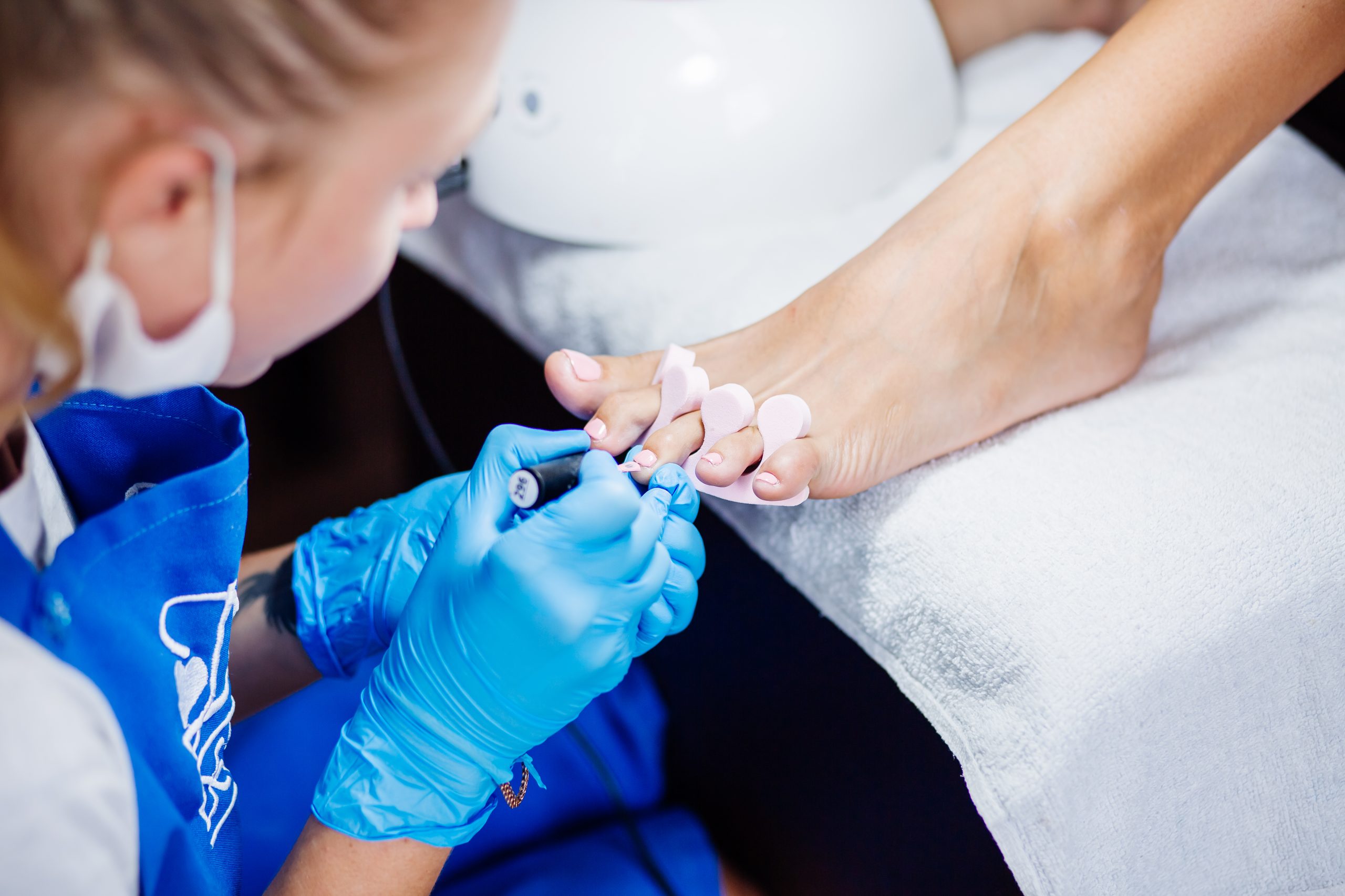 home-salon-pedicure-foot-care-treatment-nail-process-professional-pedicures-master-blue-gloves-apply-light-pink-gel-polish